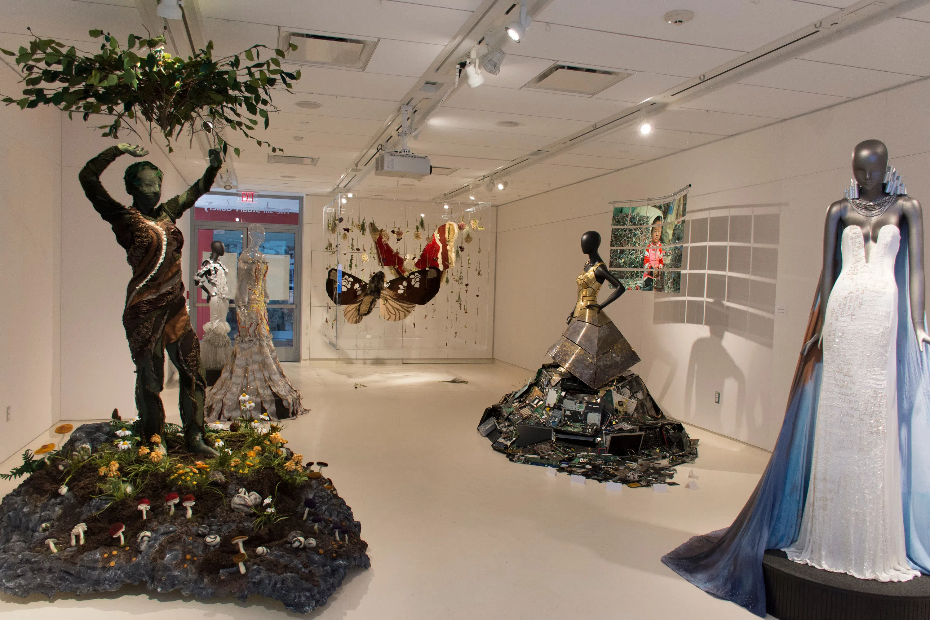 A fashion exhibit in the Jill Stuart Gallery. There are several mannequins, two of which are positioned on top of small, circular pedestals that are intricately decorated.