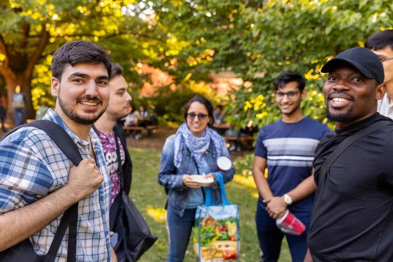 A group of graduate students smile at the camera during an outdoor gathering at the Big Red Barn.