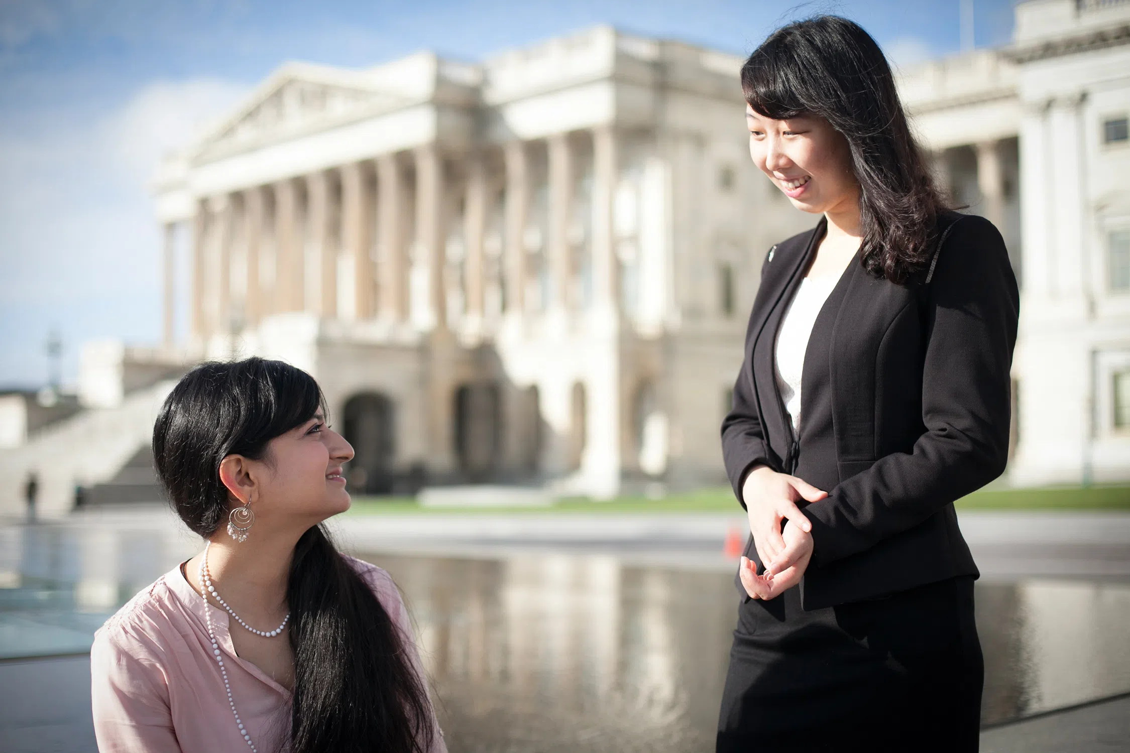 Two women in the foreground look at each other. The U.S. Supreme Court is in the background, slightly out of focus.