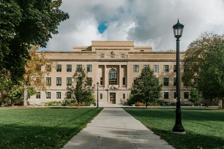 A view of Warren Hall on the Ag Quad with a lamp post on the right of the path leading to the entrance and blue sky peeking through the clouds above the building.