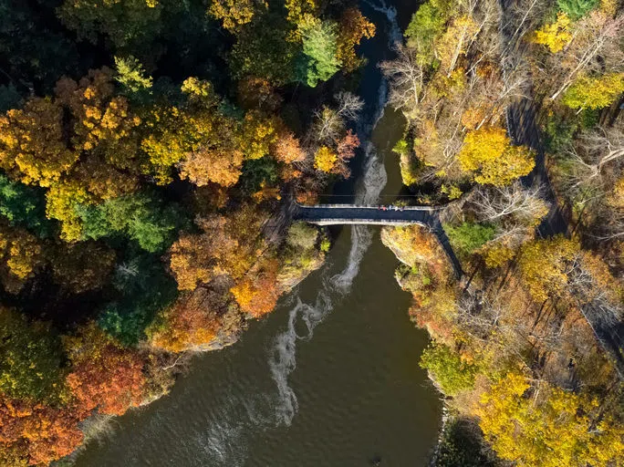 An aerial view of people crossing Sackett Footbridge over Beebe Lake, surrounded by colorful trees in autumn.