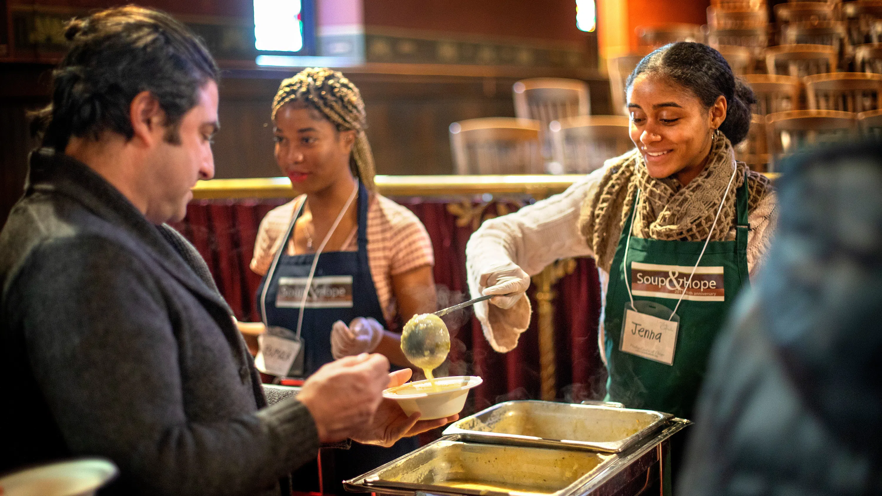 Volunteers in Sage Chapel ladle soup out from a metal container to a man holding out a bowl.