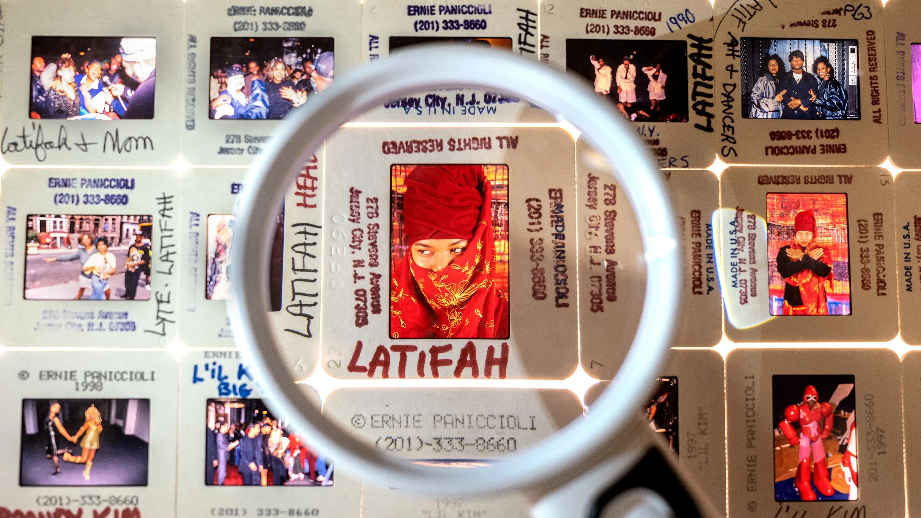 A magnifying glass is held over 35mm slides on a lightbox. Many of the 15 slides feature Queen Latifah, who is wearing a red headdress.