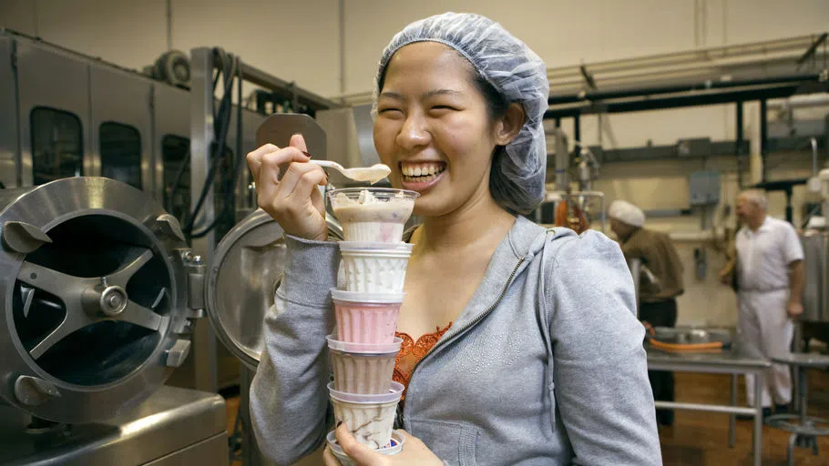 Cornell Dairy Bar Ice Cream containers stacked high in the arms of a smiling student.