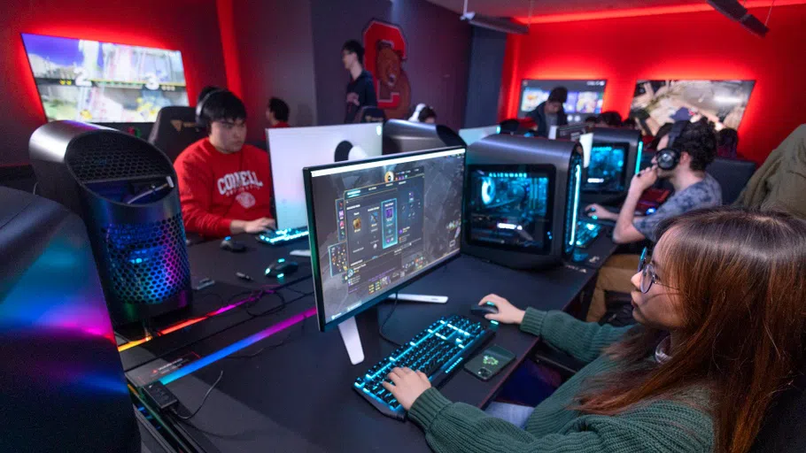 In the Esports Gaming Lounge, four students sit and stand near a console on the left, while a sole gamer uses a different console in the foreground, at right.