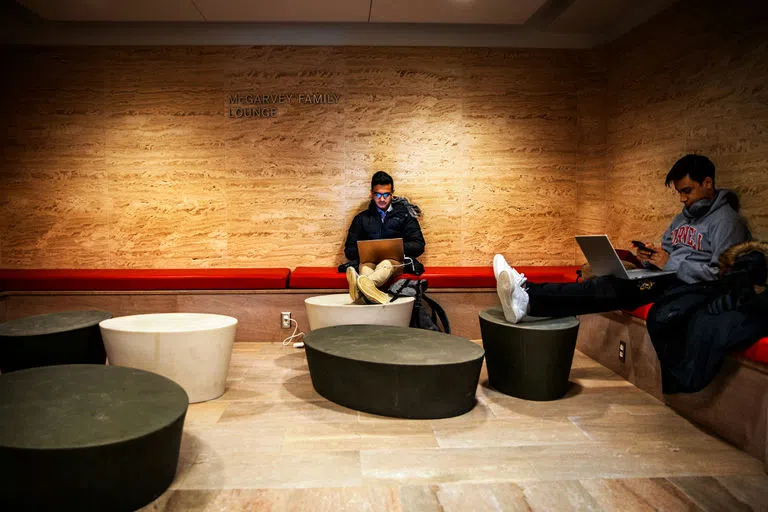 Students sit on couches with their feet up on round footstools, while they work on laptops in the McGarvey Family Lounge in Warren Hall.