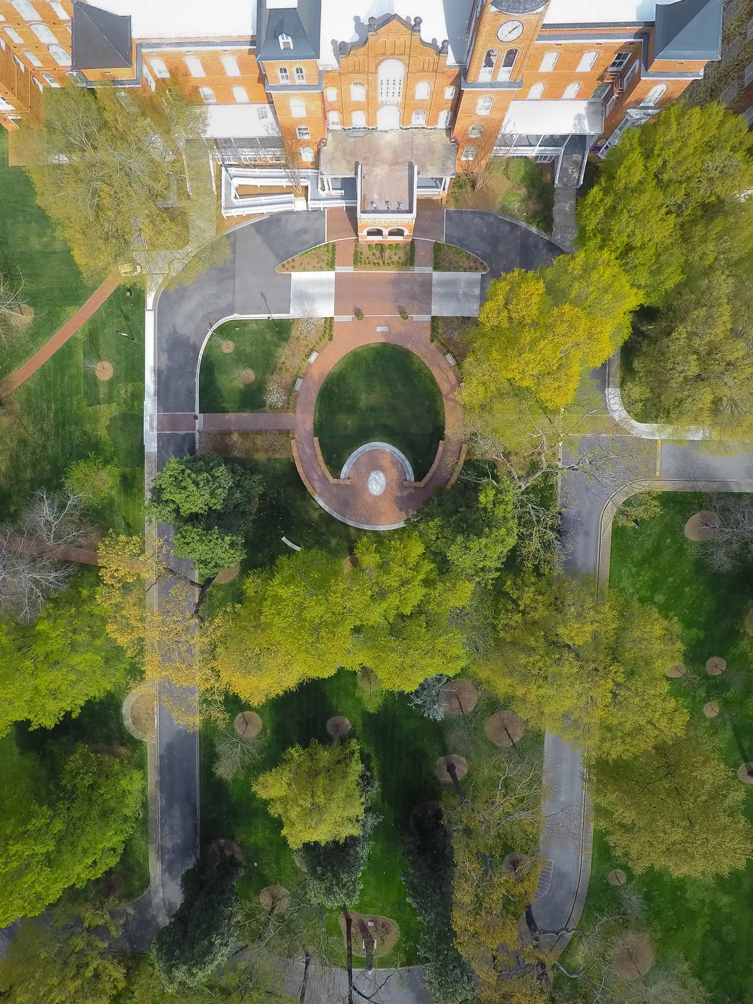 Large outdoor garden with grass and trees seen from above in image taken by drone. A large circular landing is ringed by a brick walkway. 