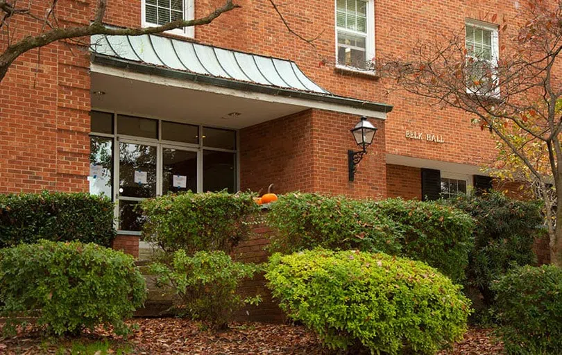 Two glass front doors covered by a copper awing lead into a brick building with words "Belk Hall".