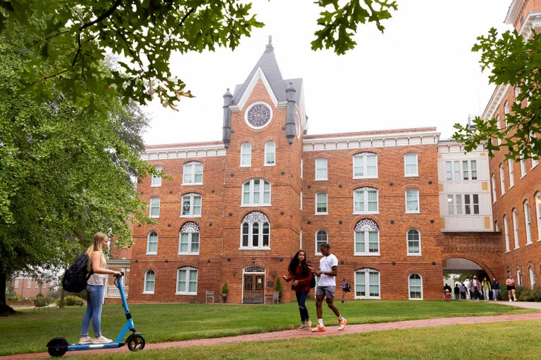 Four story brick building featuring a prominent front tower with a circular, stained-glass window at the top.