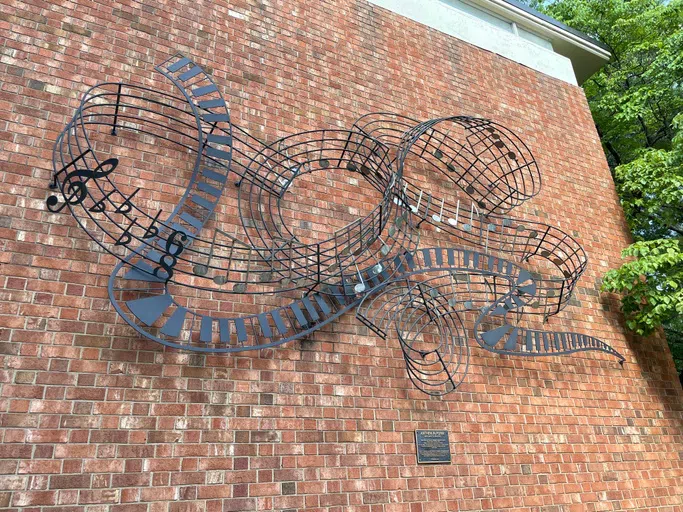 Iron and metal sculpture hangs on the outside of a brick wall.