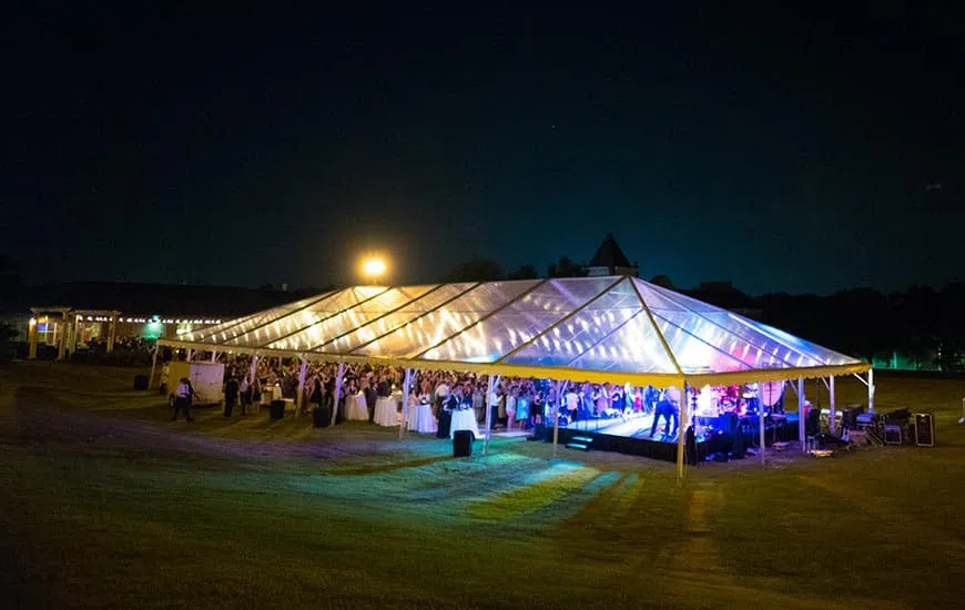 A large white event tent situated in an open outdoor green-space is illuminated in the evening .