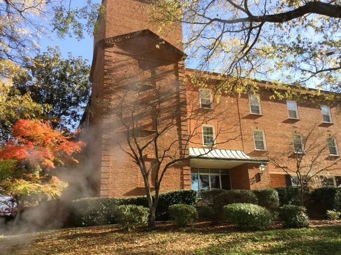 Three story brick building with grassy field in foreground.