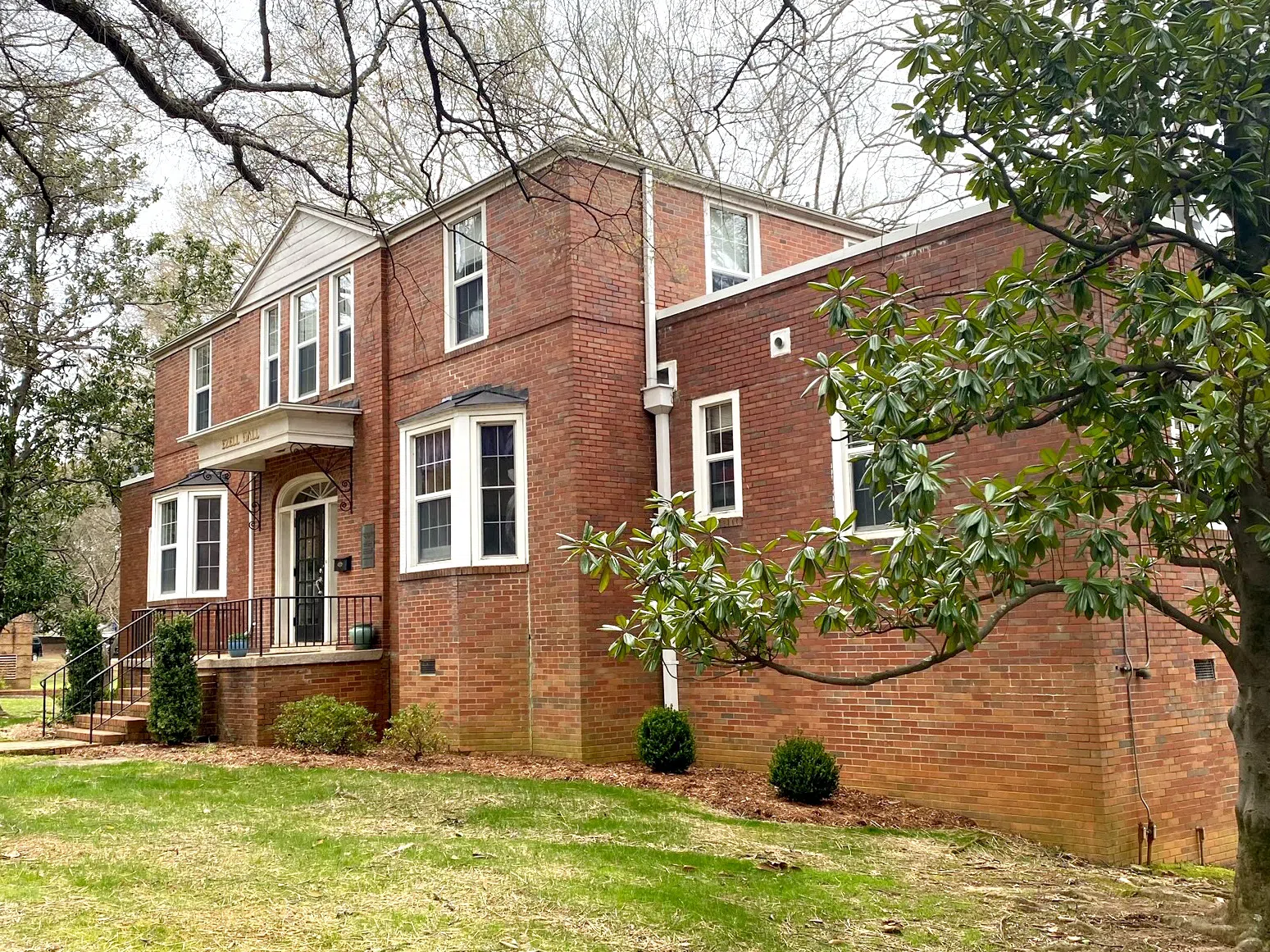 Two-story brick building with covered porch over the landing area at the top of stairs. A magnolia tree branch is seen in the foreground to the right.