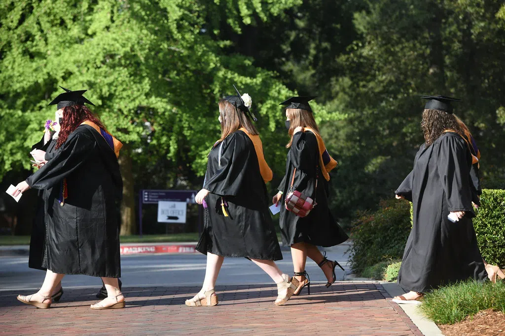 4 women cross in front of the camera in graduation caps and gowns.