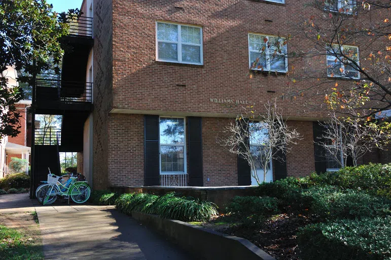 Three story brick building with argyle patterned bricks on two sides. Gold letters above the doors show "Williams Hall." Several bicycles are parked on the left side of the building.