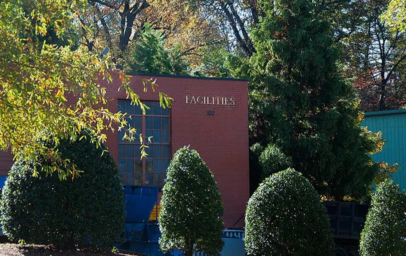 Two story brick building with a column of glass windows in the center. The word "Facilities" appears in gold letters in the upper right corner of the building. 