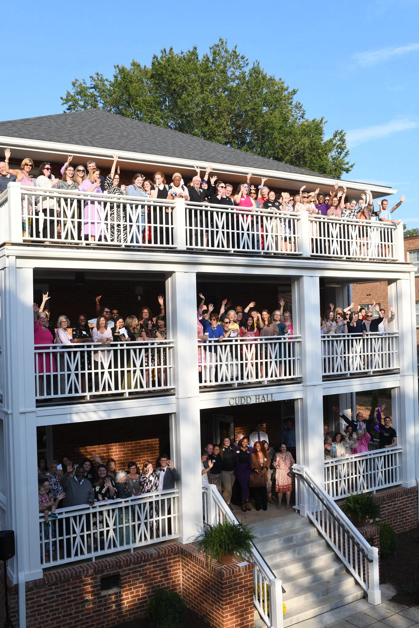 Photo shows groups of people waving from each of three porches on a brick three story building.