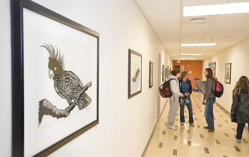 Four students with backpacks stand talking in a hallway with artwork lining the walls.