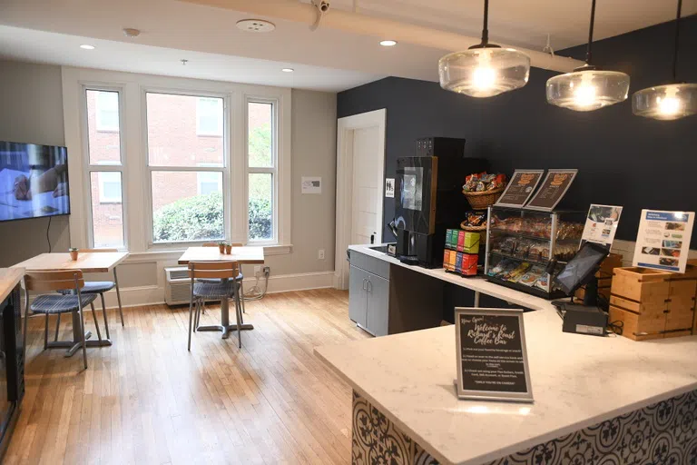 A small table and two chairs sit in front of a large window in a coffee and tea service area. A sign in the foregrounds says, "Now Open! Richard's Roast Coffee Bar"