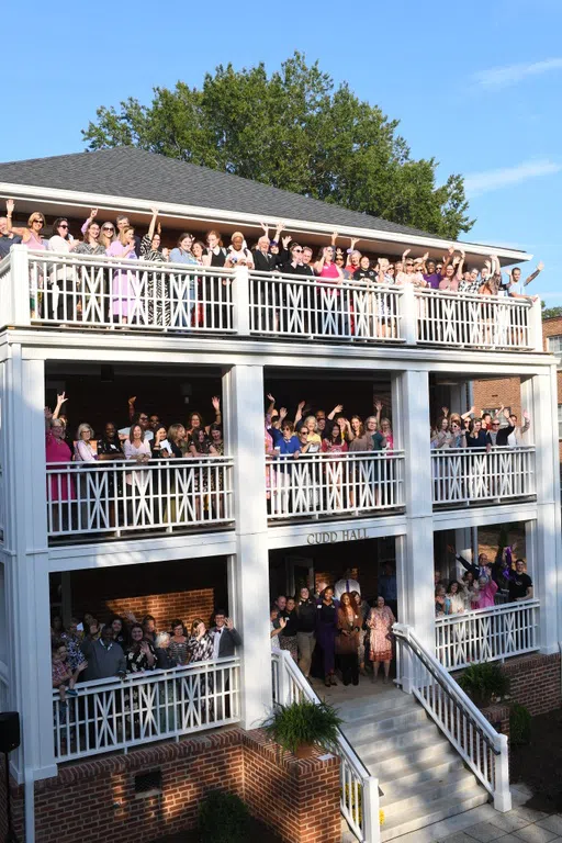 Photo shows groups of people waving from each of three porches on a brick three story building.