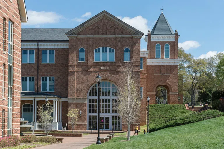 An extensive brick building with a long arched walkway sits beneath a bright blue sky