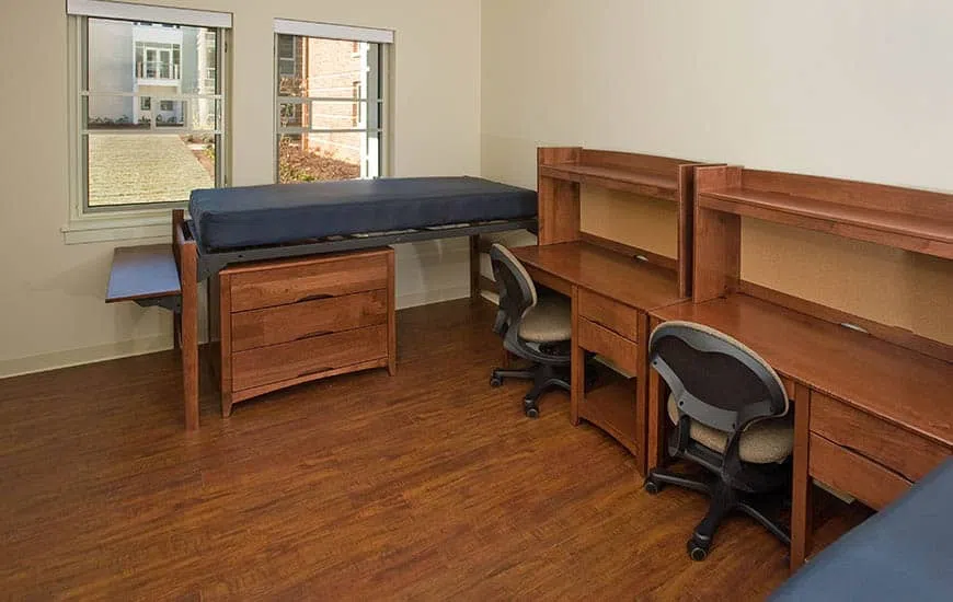 A dorm room with rich wood floors and a layout of two twin beds and two desks.