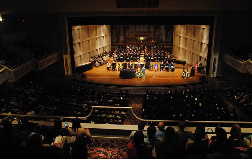 View of performance in progress with musicians on well-lit stage with audience members in seats with dimmed lights.