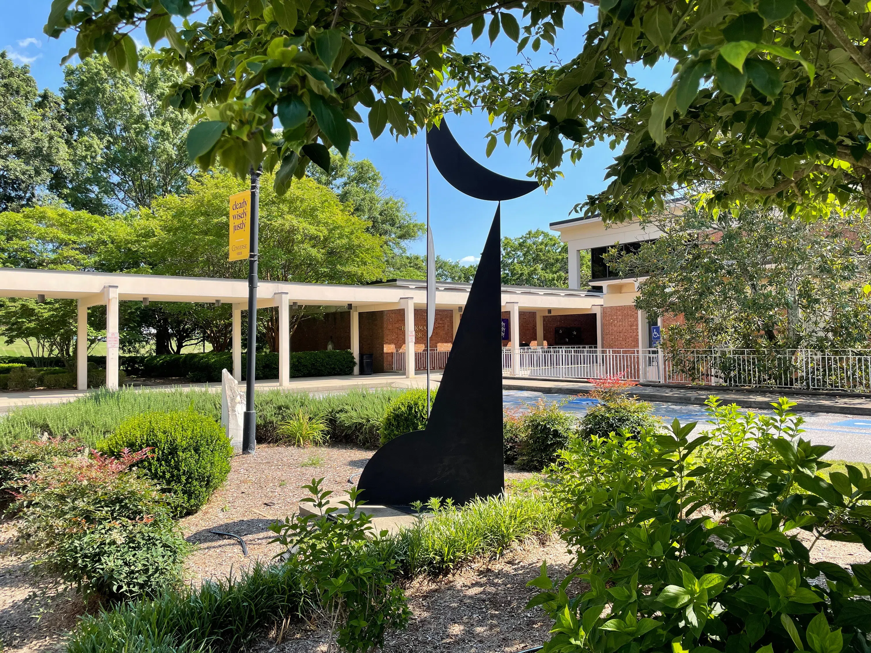 A metal, geometric sculpture appears in the foreground before a one-story building with a covered walkway.