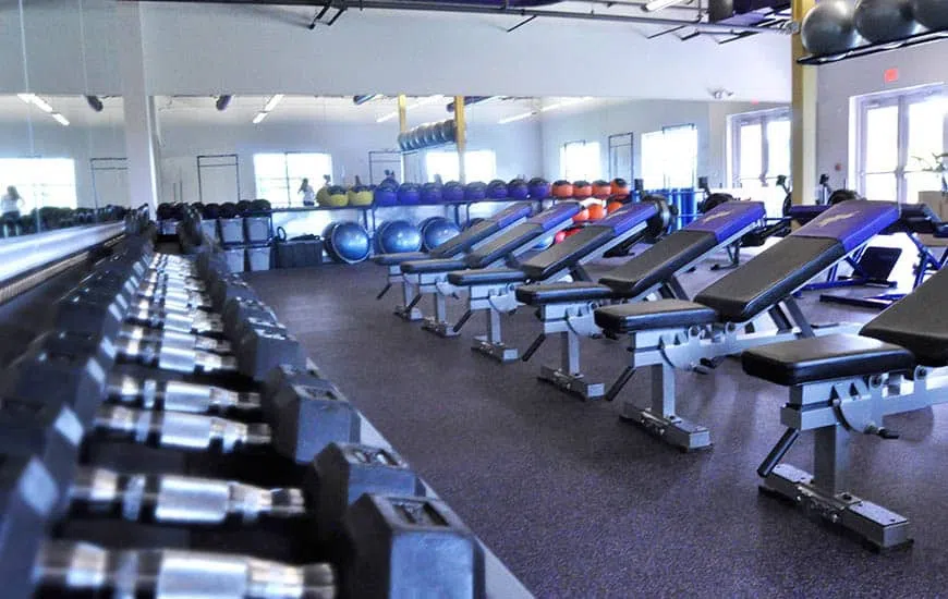 Workout equipment lines both sides of a pathway through a well-lit gym.