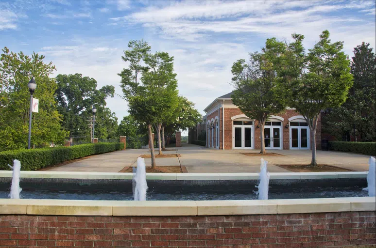 Small water fountains appears in the foreground of a one-story brick building with large windows and a courtyard.