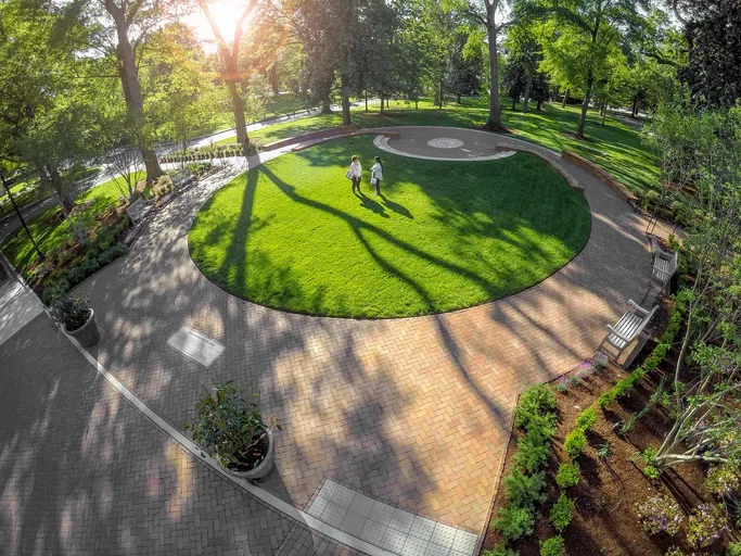 View of circular, outdoor green-space with brick walkways as seen looking down from a second story window.