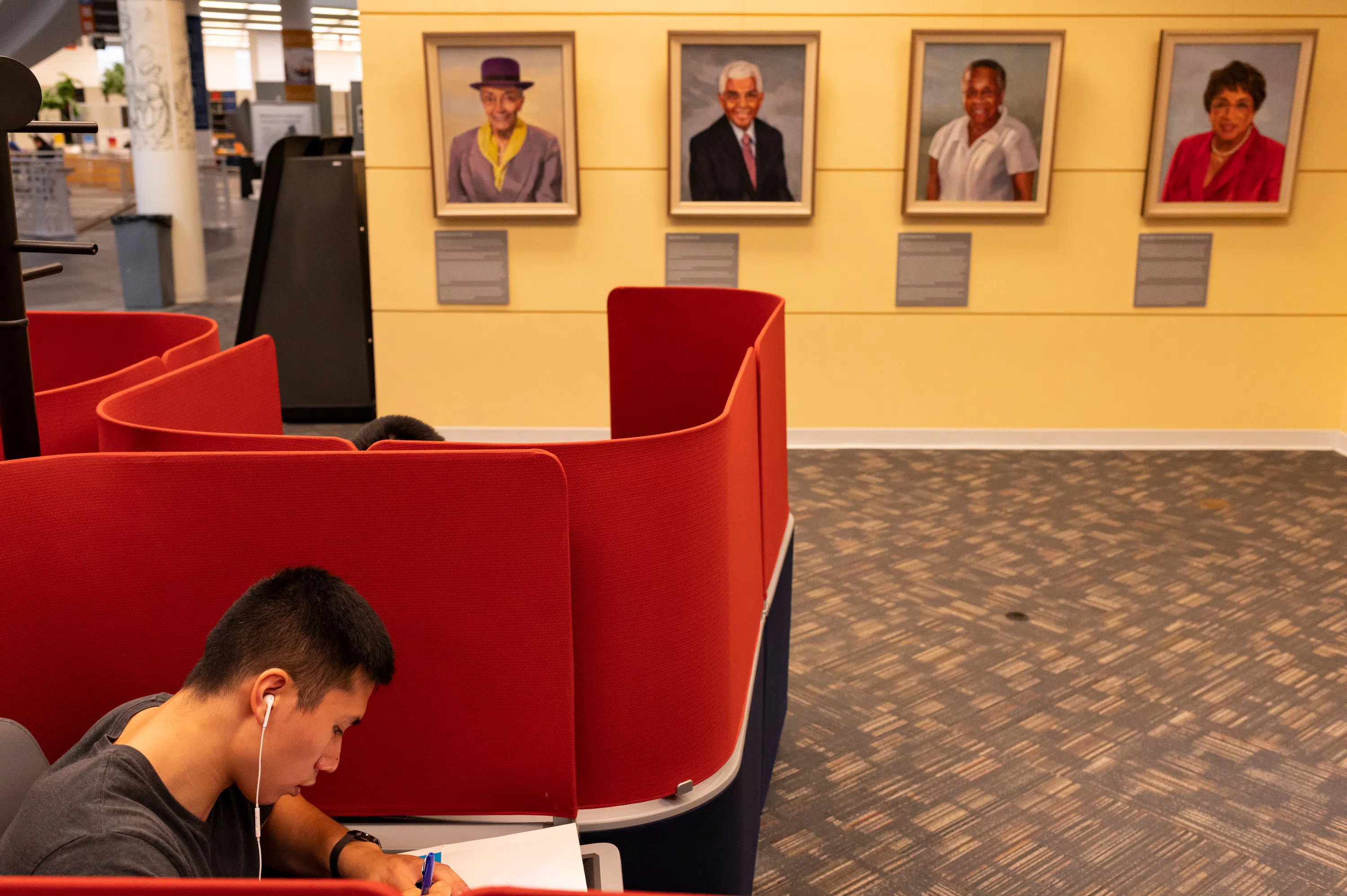 A student works in the foreground with portraits of CWRU Trailblazers hang on the wall in the background
