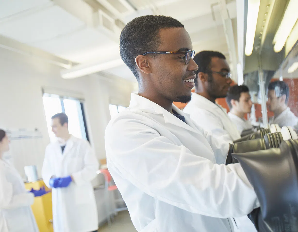 Students reach into research equipment with gloves