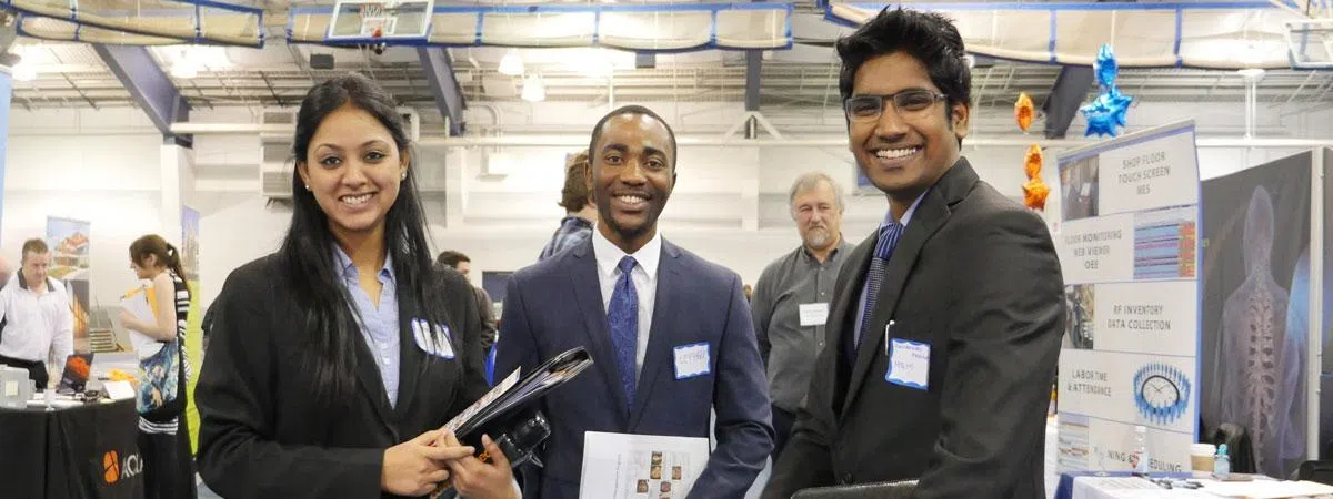 Three students dressed in business professional clothing smiling at the camera at the career fair