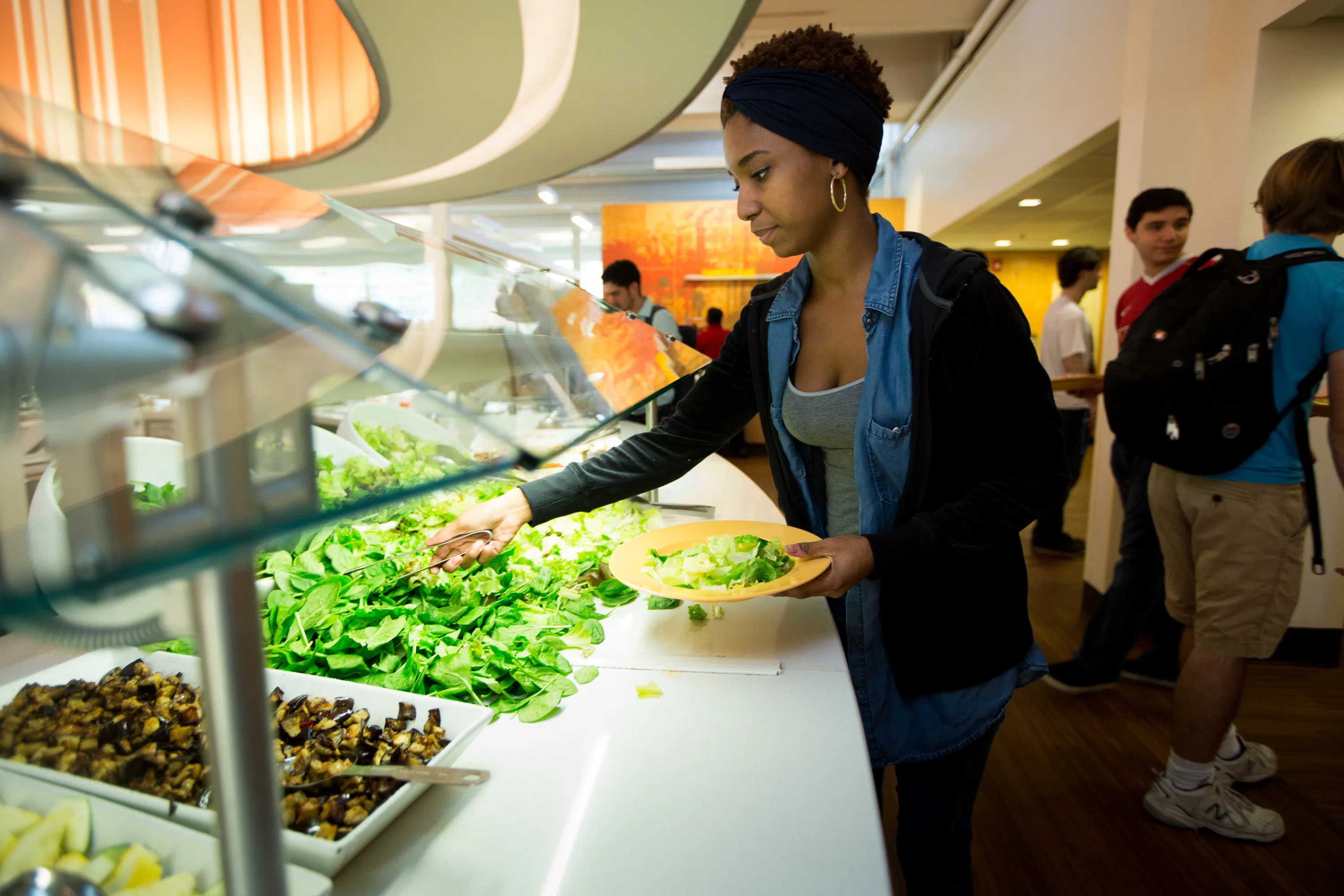 A student using tongs to get lettuce from the salad bar