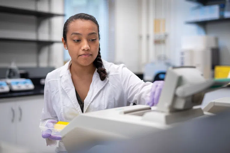 Student in lab coat with gloves working on equipment