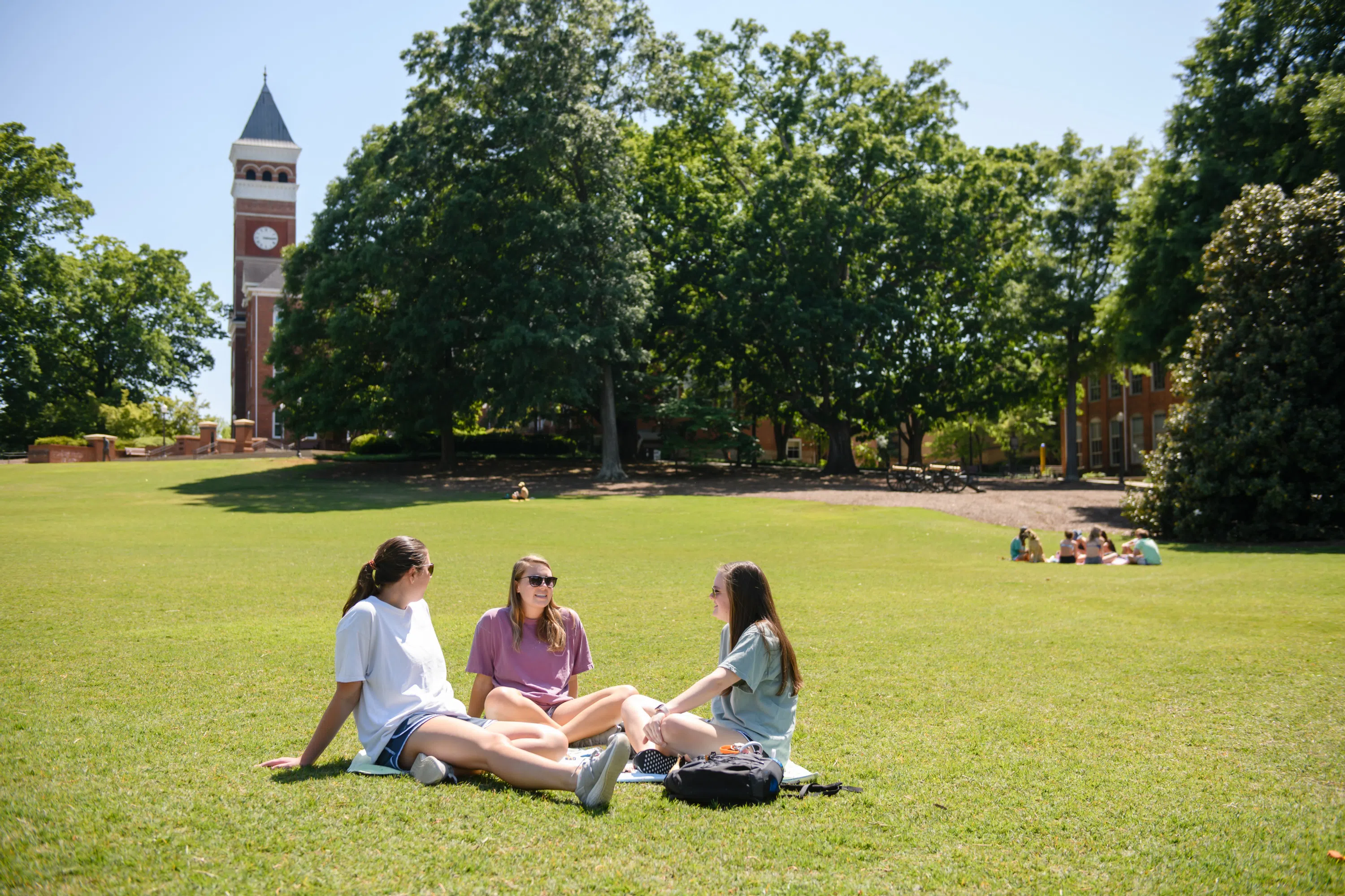 A group of three female students gathers on Bowman Field on a bright spring day.