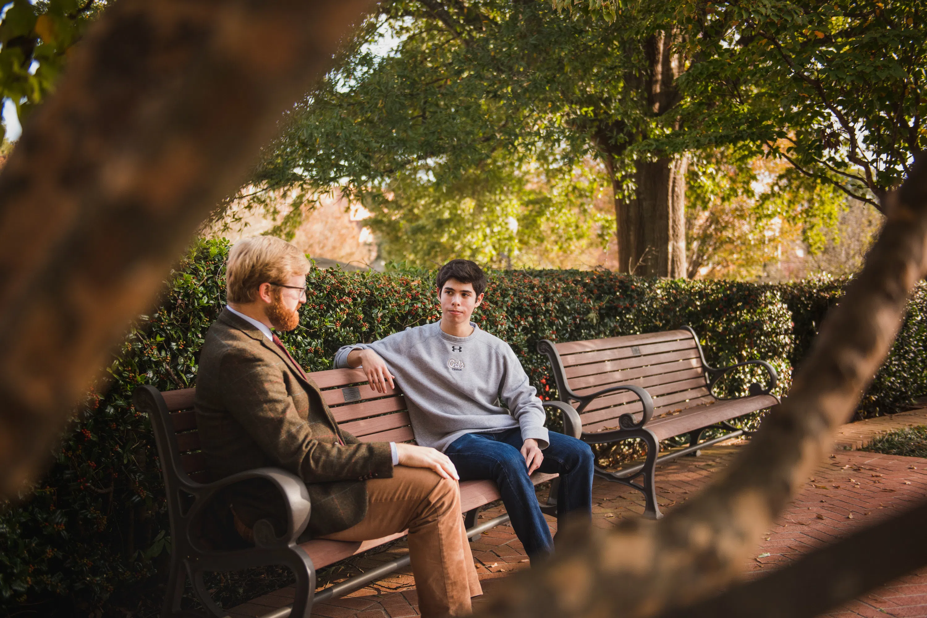 A student and his professor sit on benches in front of the Carillon Garden.