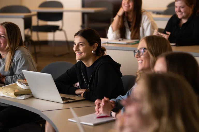 Students sitting at their desks with laptops open smiling at their professor