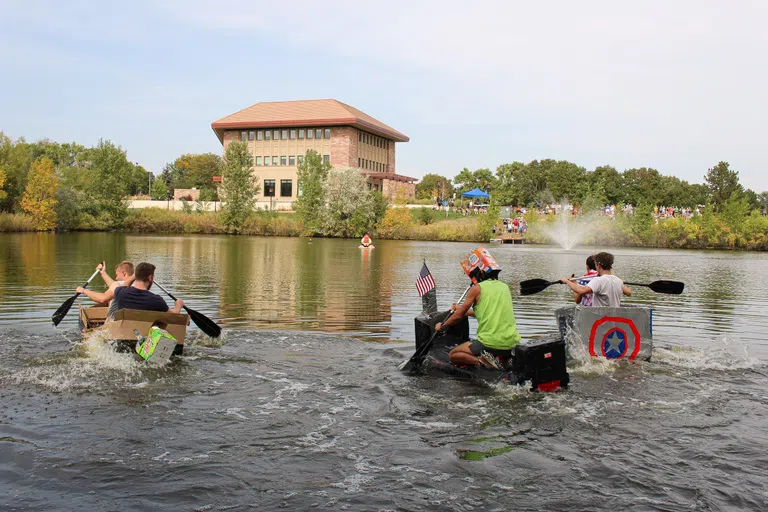 Students made boats out of cardboard and are sitting in them, paddling across the river