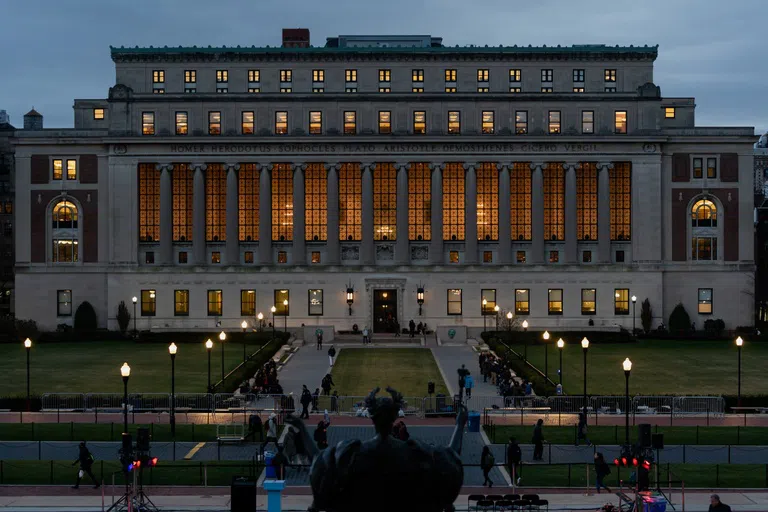 Wide shot of Butler library at dusk, campus is dimly lit with bronze Alma Mater statue in the forground