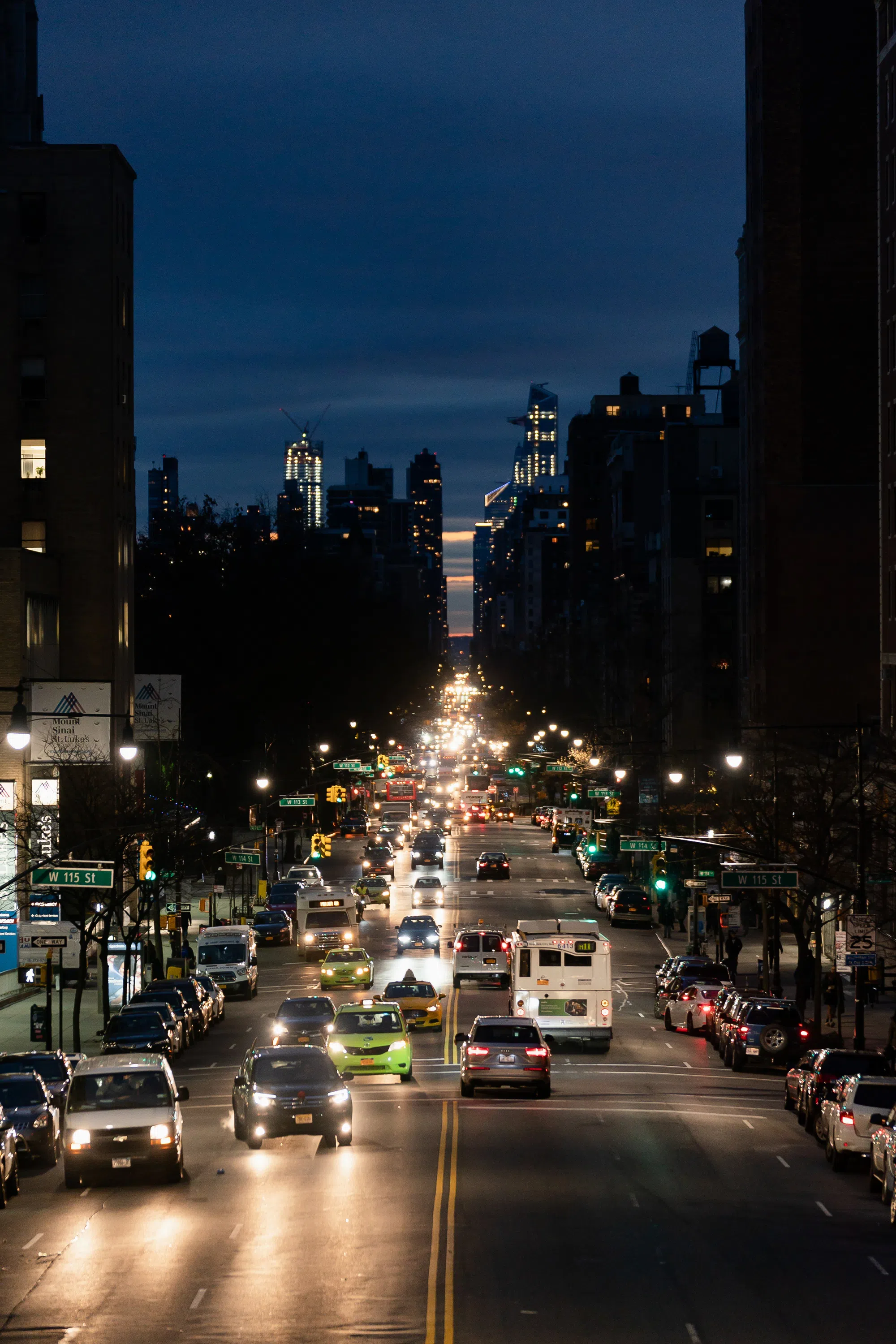 A landscape view of downtown New York City during the night time. The scene is lit with car headlights and skyscrapers.