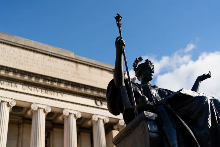 View of bronze statue of a woman sitting with a staff in her hand on a sunny day