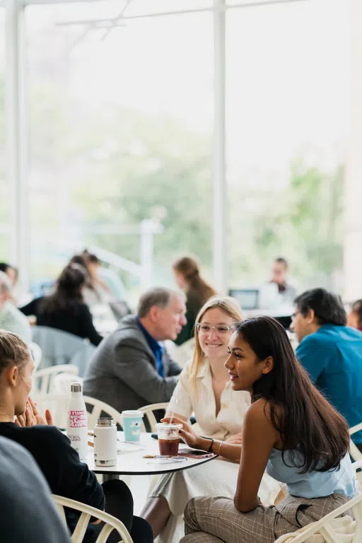 Crowded dining hall, focus is on three female students sitting at a round table.