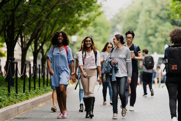 A group of student walk towards the exit of Campus on the main College Walkway