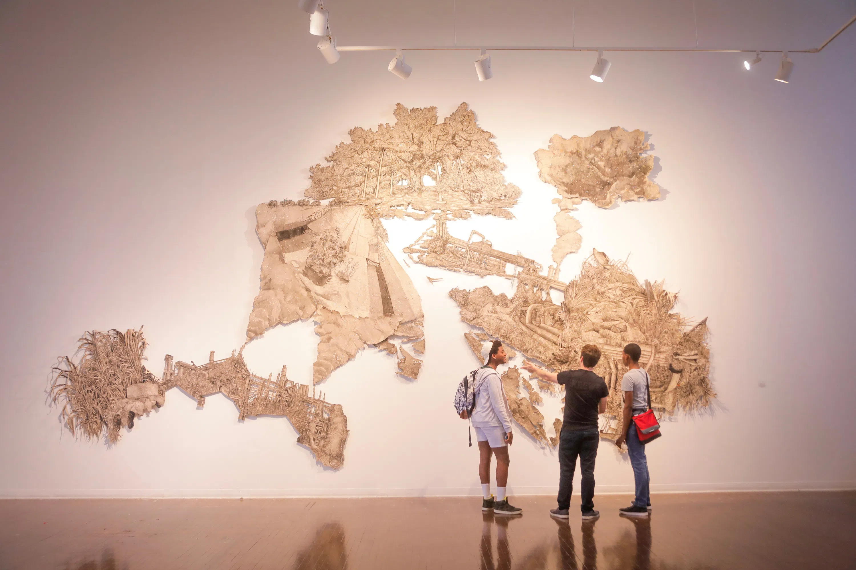 3 people looking at large map art display on wall
