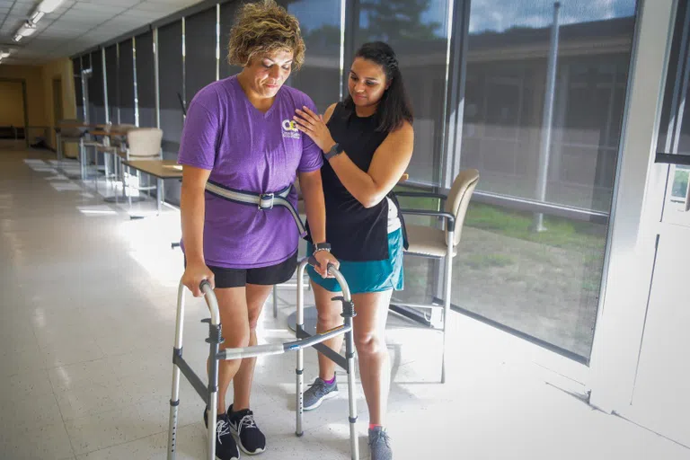 person helping another with a walker down a hallway