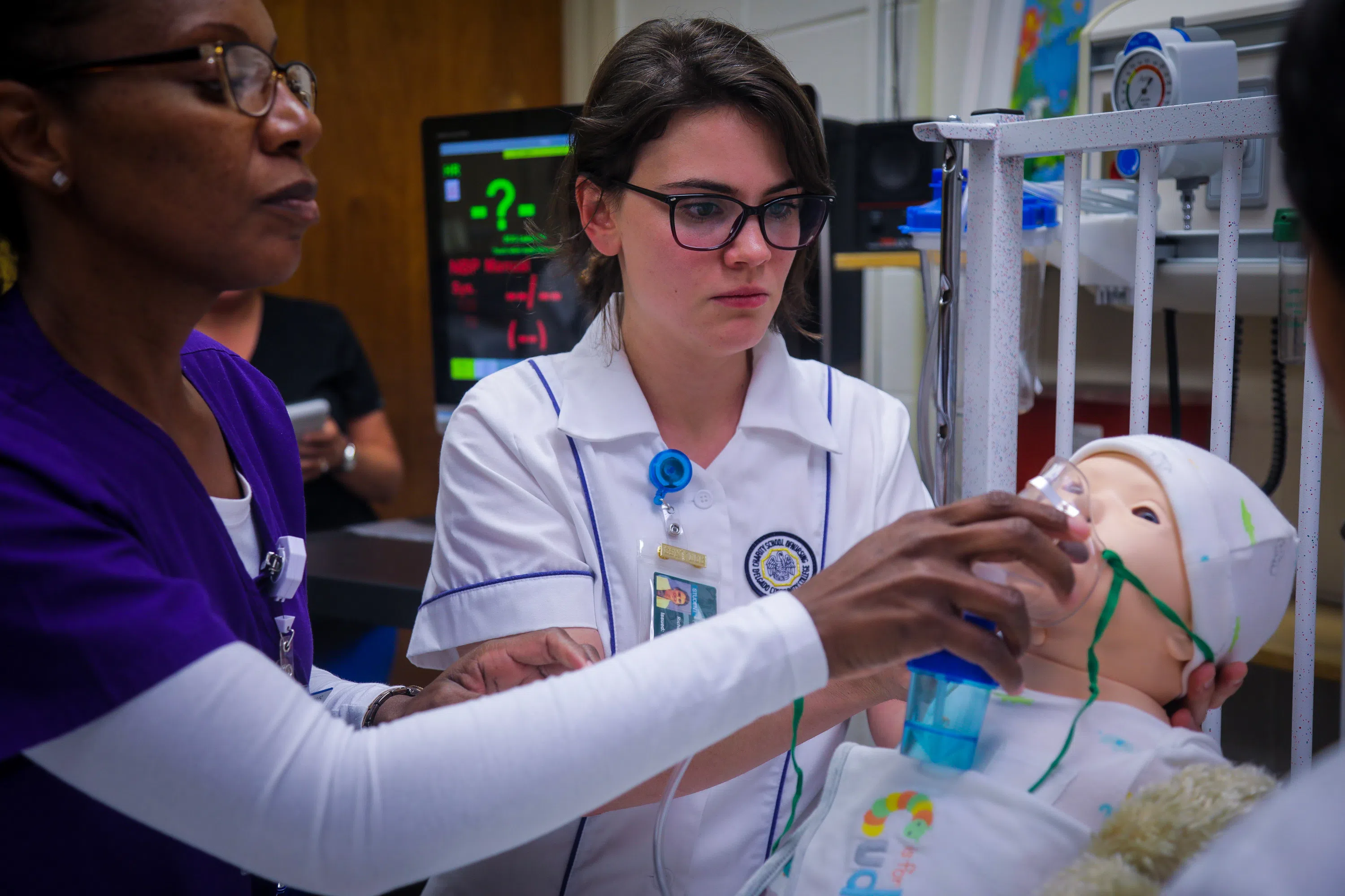 2 nursing students putting oxygen mask on baby practice dummy