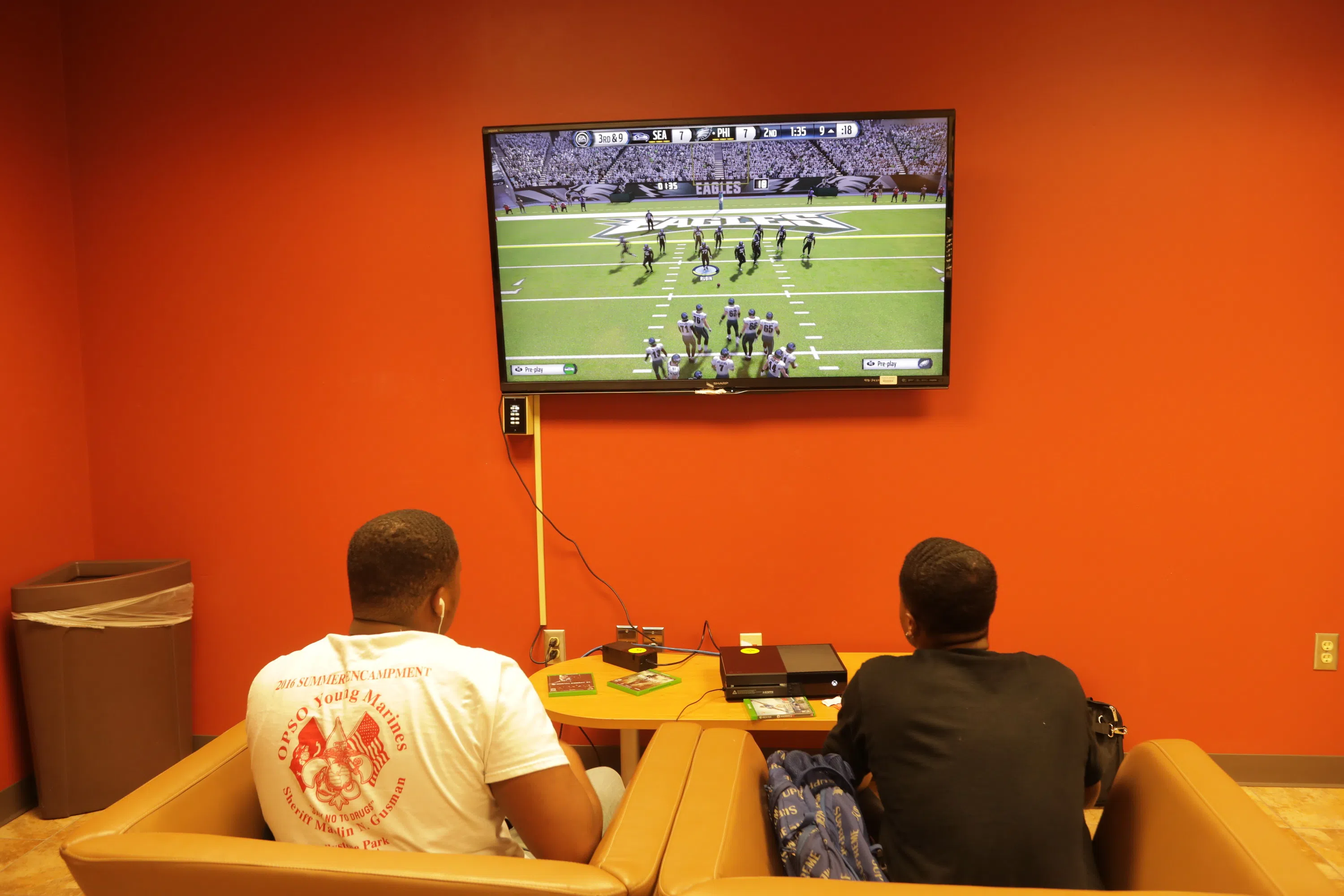 2 people facing a large tv mounted to a wall playing video games