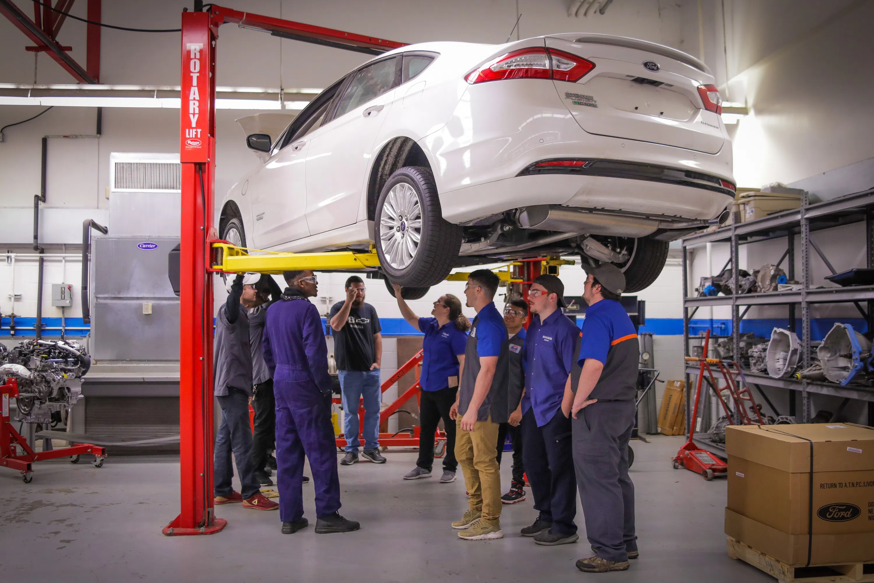 multiple students looking at the underside of a car up on a lift